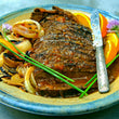 Load image into Gallery viewer, 100% grass-fed and field harvested bison brisket with orange glaze on a blue and yellow plate with a butter knife