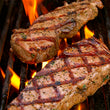 Load image into Gallery viewer, 100% grass-fed and field harvested bison new york strip steaks on a grill