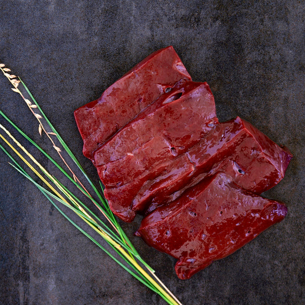 Raw liver slices on a black background next to prairie grass