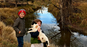 Two children holding a cat in front of a river