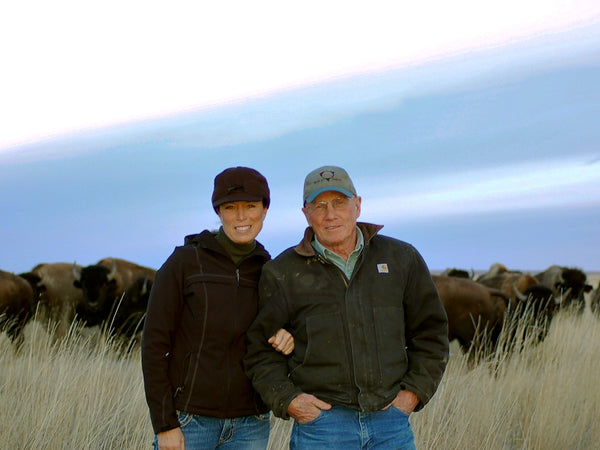 Dan and Jill in front of buffalo herd wearing coats and hats