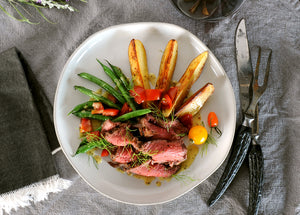 Sliced bison steak with potatoes and green beans on a plate.