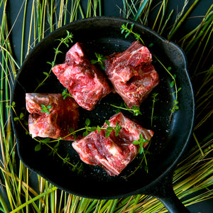 100% grass-fed and field harvested bison meaty bones in a black skillet with thyme