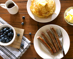 100% grass fed and field harvested bison breakfast sausage links on a wooden table with pancakes, blueberries, and syrup.