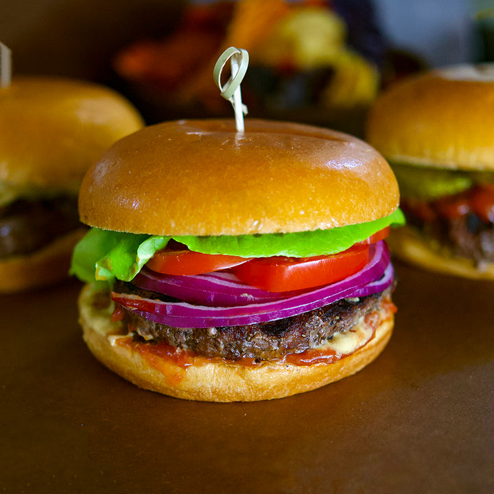 100% grass-fed and field harvested buffalo burger with lettuce, tomato, and onion on a plain table