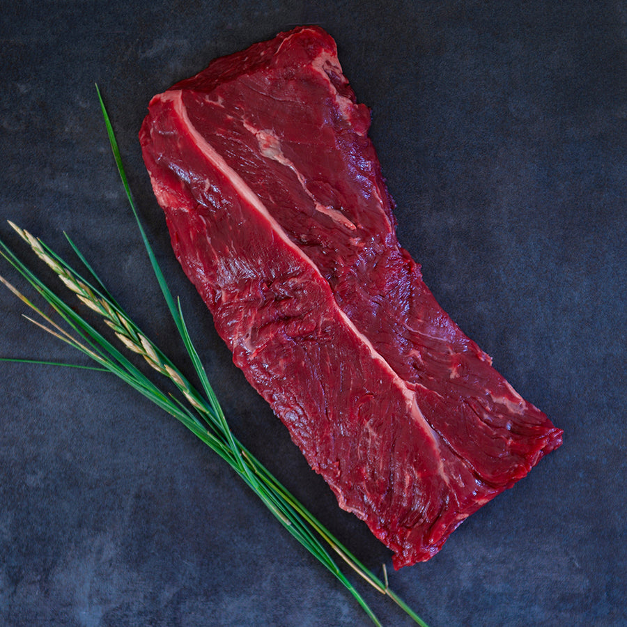 100% grass-fed and field harvested bison hanger steak on a black background