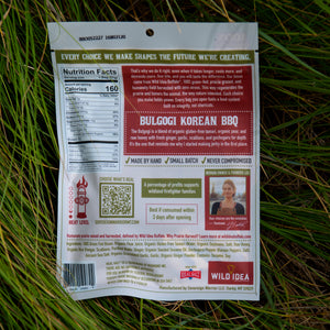 Back of a Bulloggi Korean BBQ steak package, photographed lying on green grass outdoors. The package is mostly white with a large dark red back panel containing product information, a QR code, ingredient list, and branding.