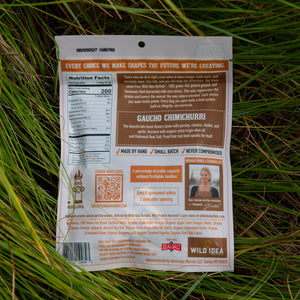 The back of a Wild Idea Gauchó Chimichurri seasoning packet, showing nutrition facts, ingredients, and customer testimonials, photographed lying on a grassy outdoor surface.