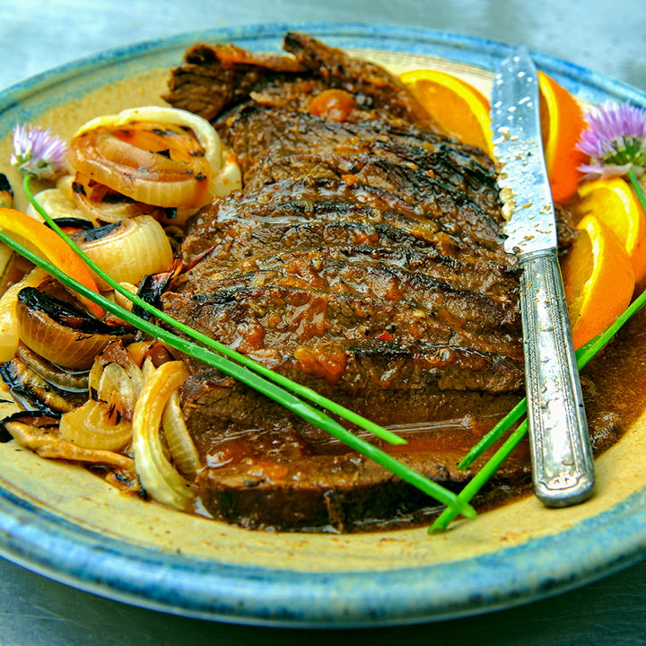 100% grass-fed and field harvested bison brisket with orange glaze on a blue and yellow plate with a butter knife