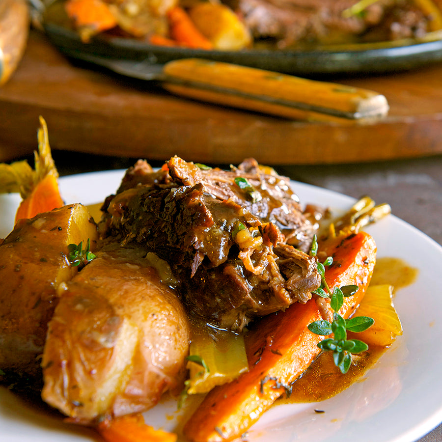 100% grass fed and field harvested bison chuck roast slow roasted in gravy and plated on top of potatoes and carrots on a white plate