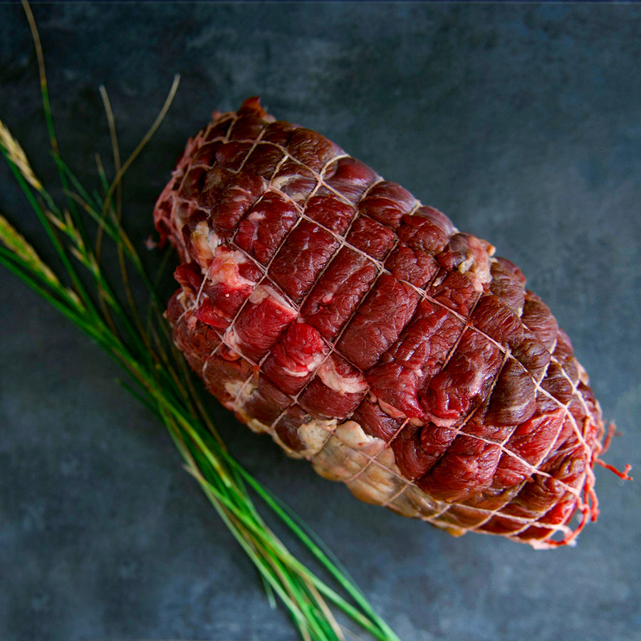 100% grass fed and field harvested raw bison chuck roast in a net on a black background