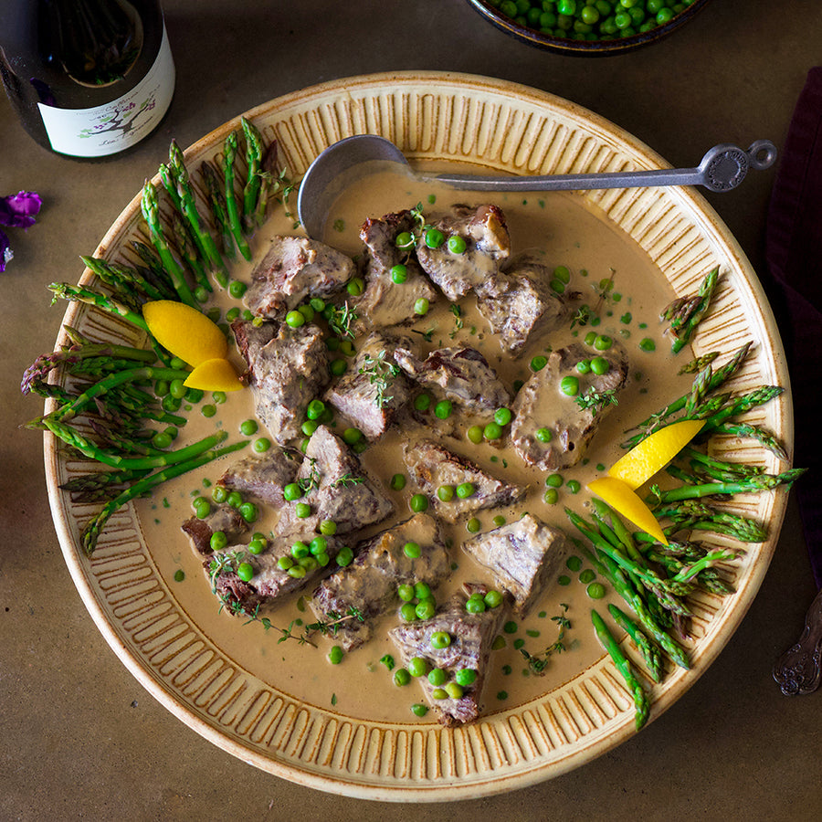 100% grass fed and field harvested bison chuck roast braised in milk with peas and asparagus on a white plate