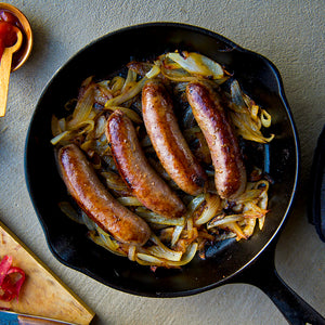100% grass-fed and field harvested buffalo bratwurst searing in a black cast iron skillet with onions