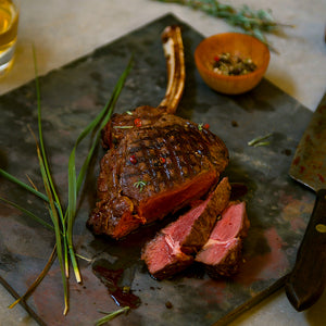 100% grass-fed and field harvested grilled bison bone-in ribeye on a black cutting board