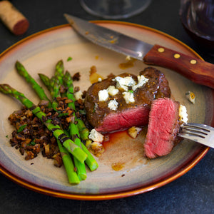100% grass fed and field harvested seared buffalo tenderloin filet with asparagus on a grey plate with a fork and knife