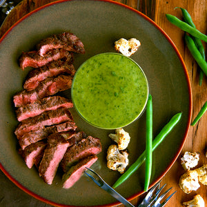 100% grass fed and field harvested buffalo flat iron steak on a plate with green bagna cauda sauce 