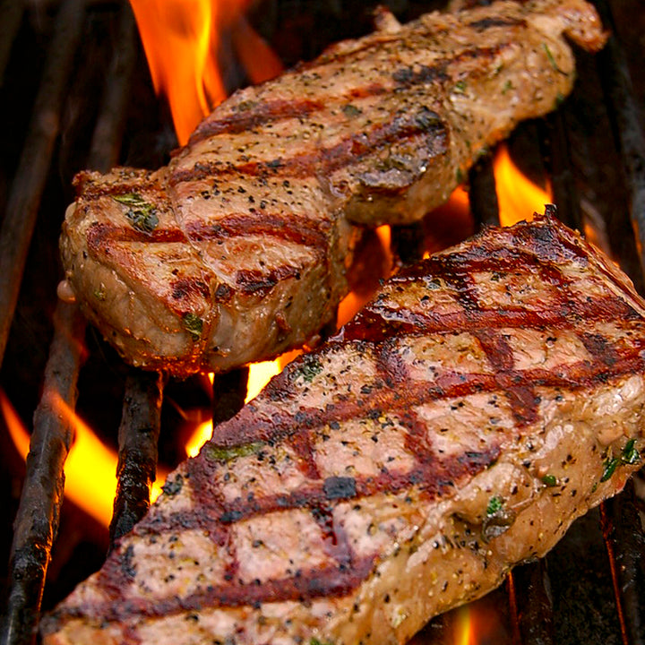 100% grass-fed and field harvested bison new york strip steaks on a grill