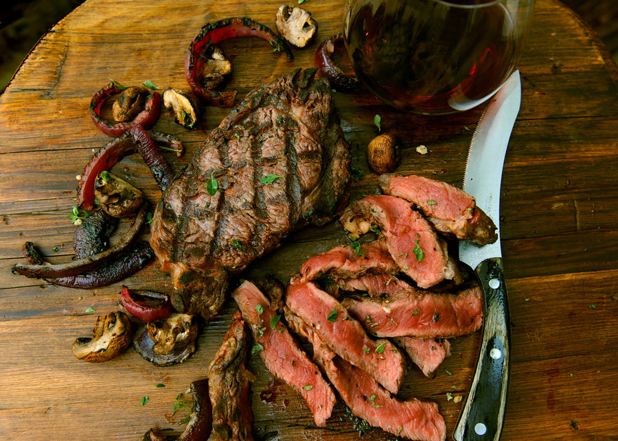 Grilled steak with sliced pieces on a wooden cutting board, accompanied by mushrooms and a glass of red wine.