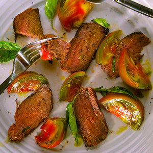 100% grass-fed and field harvested sliced bison sirloin steak with tomatoes on a white plate