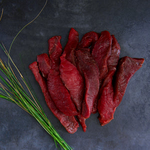 100% grass-fed and field harvested raw bison steak strips on a black background