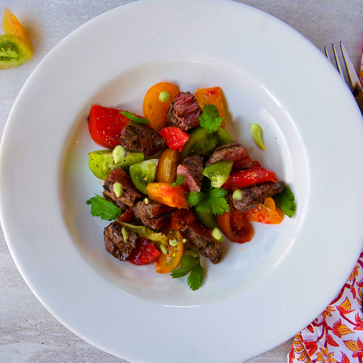 100% grass-fed and field harvested bison tenderloin tips with heirloom tomatoes on a white plate