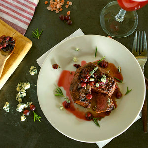 100% grass-fed and field harvested bison top sirloin steak with champagne grapes on a white plate