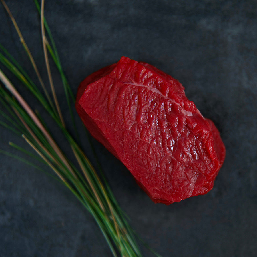 100% grass-fed and field harvested raw bison top sirloin steak on a black background