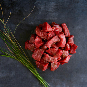 100% grass-fed and field harvested raw bison stew meat on a black background