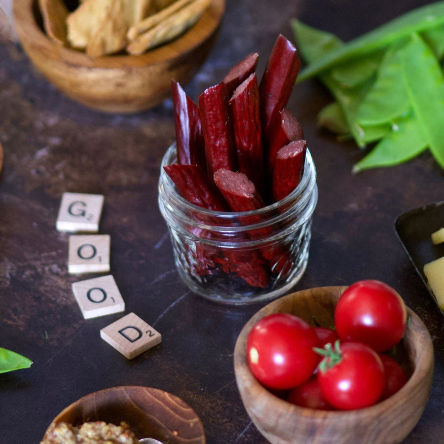 100% grass-fed and field harvested bison snack sticks in a jar with tomatoes and scrabble tiles reading "good"